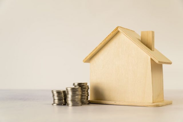 casita de madera con monedas a un lado